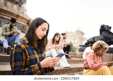 Group of individualistic people using phone outdoors with serious face. Friends focused on their mobiles sitting on a staircase in a city. Technology addicts concept. High quality photo - Powered by Shutterstock