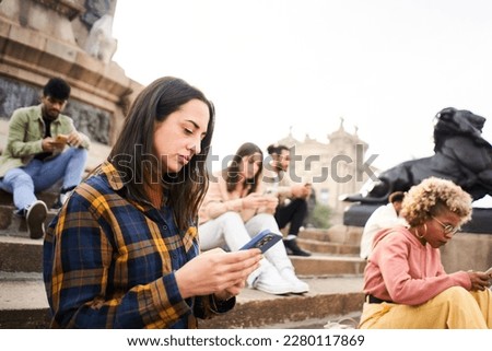 Group of individualistic people using phone outdoors with serious face. Friends focused on their mobiles sitting on a staircase in a city. Technology addicts concept. High quality photo
