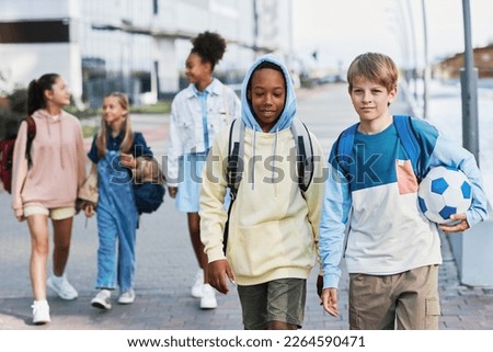 Group of intercultural adolescent secondary school learners in casualwear walking along street while going home after classes