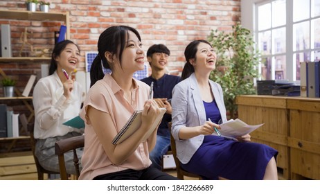 Group Of Interested Audience Laughing And Listening To Colleague Report In Bright Boardroom In The Morning.