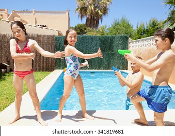 Group of joyful children playing by swimming pool in a home garden on a sunny summer holiday, having fun with water pistols outdoors. Active kids lifestyle, playing in house exterior on vacation.