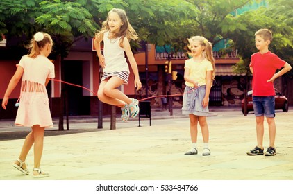 group of joyful children skipping together with jumping rope on urban playground