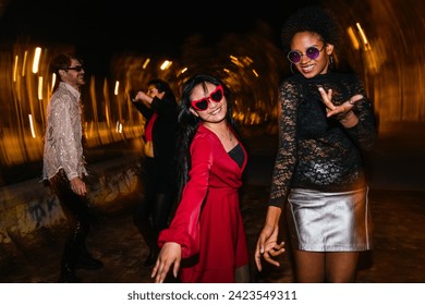 Group of joyful diverse friends dancing outdoors at night. Light painting streaks capture the lively party atmosphere. - Powered by Shutterstock