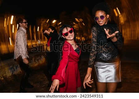 Group of joyful diverse friends dancing outdoors at night. Light painting streaks capture the lively party atmosphere.