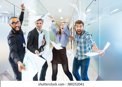Groupe d'hommes d'affaires joyeux et excités jetant des papiers et s'amusant au bureau