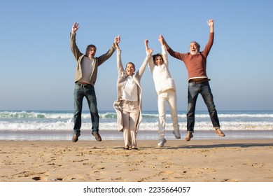 Group of joyful senior friends having fun at beach on sunny autumn day. Four people laughing and jumping up high while raising their arms in triumph. Vacation, joy, friendship, retirement concept - Powered by Shutterstock