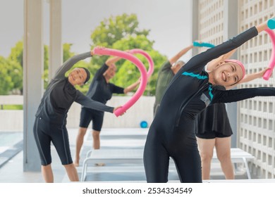 group of joyful seniors participates in a fun water exercise class outdoors, using colorful pool noodles for stretching and balance. They are engaged in a fitness routine, staying active and healthy. - Powered by Shutterstock