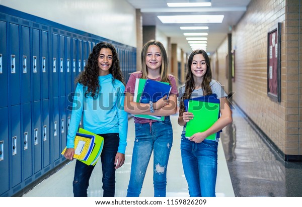 Group of Junior High school Students\
standing together in a school hallway. Female classmates smiling\
and having fun together during a break at\
school