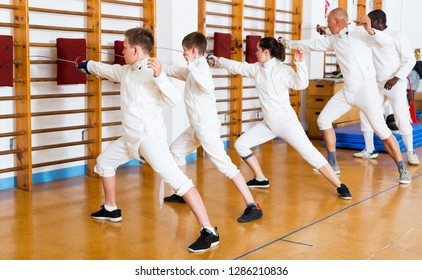 Group of kids with adults practicing effective techniques of fencing in gym
