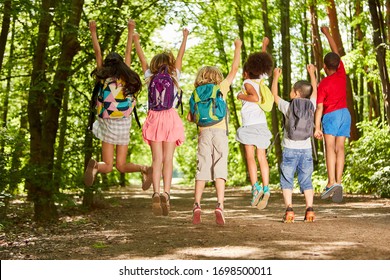 Group Of Kids With Backpacks In Nature In Summer Jumps In The Air