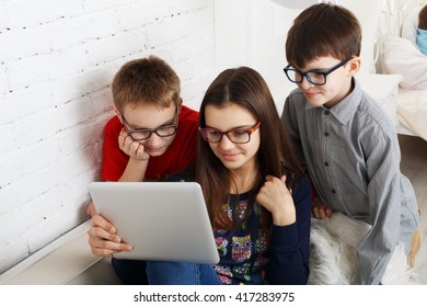 Group Of Kids In Eye Glasses Look Into Tablet. Children Computer Games, Social Networks And Media Addiction Concept. Girl And Boys With Tablet. Communication Problems