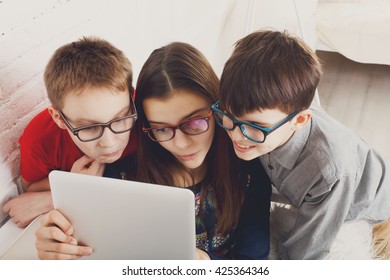 Group Of Kids In Eye Glasses Look Into Tablet. Children Computer Games, Social Networks And Media Addiction Concept. Girl And Boys With Tablet. Communication Technologies. Eyesight, Eyewear For Kids.