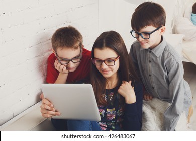 Group Of Kids In Eye Glasses Look Into Tablet. Children Computer Games, Social Networks And Media Addiction Concept. Girl And Boys With Tablet. Communication Technologies. Eyesight, Eyewear For Kids.