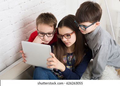 Group of kids in eye glasses look into tablet. Children computer games, social networks and media addiction concept. Girl and boys with tablet. Communication technologies.