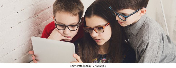 Group Of Kids In Eye Glasses Look Into Tablet. Children Computer Games, Social Networks And Media Addiction Concept. Girl And Boys With Gadget. Communication Technologies.