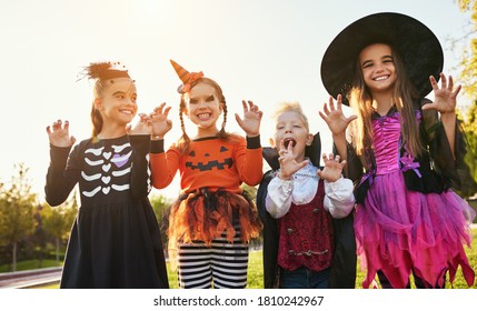 Group Of Kids In Halloween Costumes Gesticulating And Making Scary Faces Against Cloudless Sky In Park
