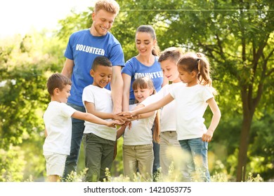 Group of kids joining hands with volunteers in park - Shutterstock ID 1421053775