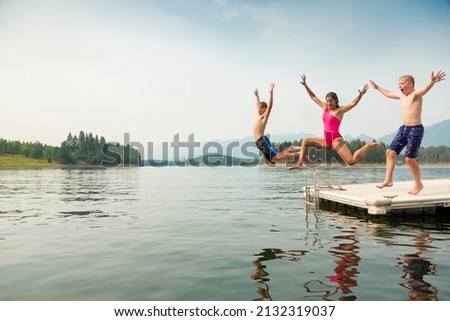 Group of kids jumping off the dock into the lake together during a fun summer vacation.	