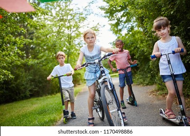 Group Of Kids Riding Bike And Scooter Together In The Park