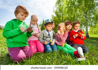 Group of kids sit in the field with magnifier