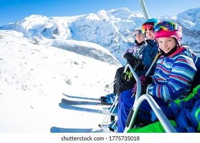 Group Of Kids Ski Friends Sit On Chairlift Lifting On The Mountain Top Peak On Sunny Day