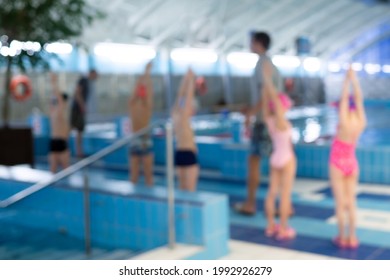 Group Of Kids At Swimming Pool Make Warm Up And Stretching Before Exercising In The Water. Blurred, Defocused Swimming Training