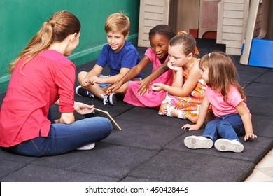 Group Of Kids Talking About Book With Nursery Teacher In Preschool