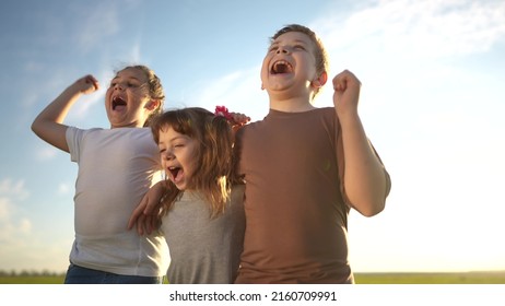 Group Of Kids Team Hugging A Jumping And Rejoicing Outdoors. Happy Family Teamwork Kid Dream Concept. Family Children Sisters Brothers Have Fun Hugging Sun In The Park In Nature