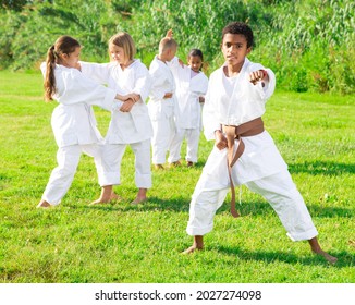 Group of kids training karate moves outdoors. African-american boy in kimono posing in foreground.