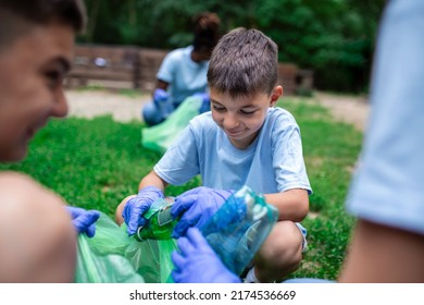 Group Of Kids Volunteers Cleaning Together A Public Park. They Are Picking Up Garbage.