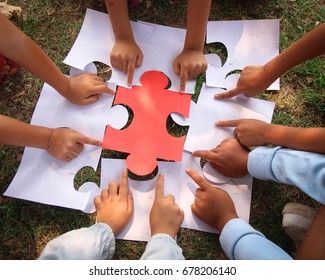 Group kids/children hands holding jigsaw/ puzzles pieces on grass/red piece center.concept: cooperation, teamwork, learning, activity, business, working, helping, diverse, education, school, playing.