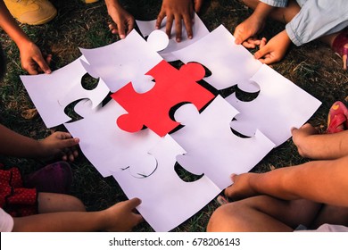  Group Kids/children Hands Holding Jigsaw/ Puzzles Pieces On Grass/red Piece Center.concept: Cooperation, Teamwork, Learning, Activity, Business, Working, Helping, Diverse, Education, School, Playing.