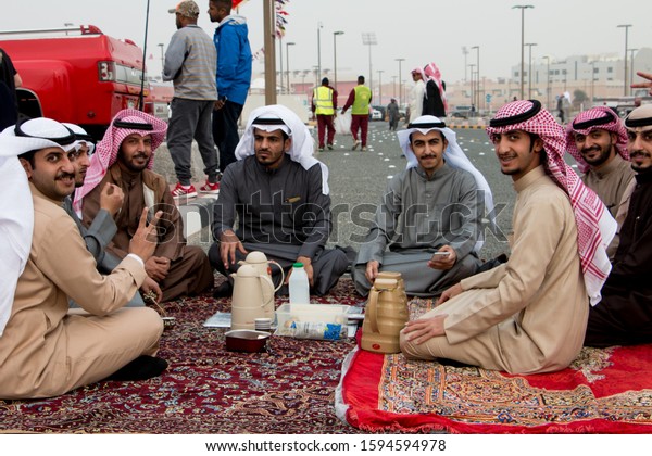 A group of Kuwaiti men dressed in dishdashas\
enjoying a cup of arabic coffee spiced with cardamom when\
exhibiting their vintage GMC trucks at a show for vintage and retro\
pickups. January 31, 2017