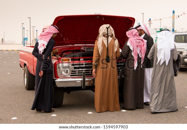 A group of Kuwaiti men dressed in winter\
dishdashas exhibiting their vintage GMC trucks at a show for\
vintage and retro pickups. January 31,\
2017