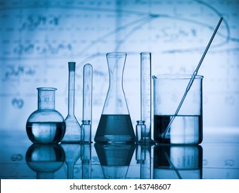 Group of laboratory flasks empty or filled with a clear liquid on blue tint scientific graphics background and their reflection on a table