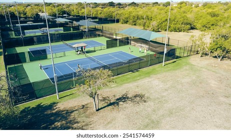 Group of ladies in sportwear practicing tennis lesson in lighted court sport complex Dallas Texas, well-lit hard courts with shaded spectator areas and comfortable benches, ball machine, aerial. USA - Powered by Shutterstock