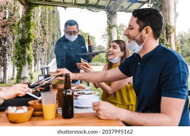 Group Of Latin Friends With Masks On The Terrace Of Mexican Restaurant Or Bar Attended By A Waiter With Face Mask. Social Distancing During Coronavirus Pandemic