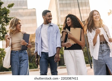 Group laughing young students with study items are walking along street, university building is in background. All interracial friends wear casual clothes. Lifestyle concept - Shutterstock ID 2202087411