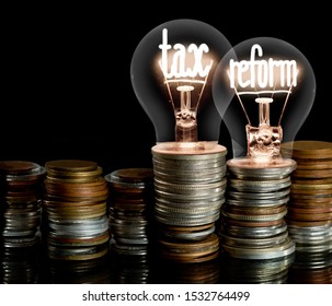 Group of light bulbs on coin stacks with shining fibers in a shape of Tax Reform concept related words isolated on black background