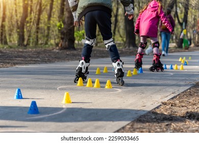 Group of little children enjoy having fun learning inline roller skate slalom with plastic cones on road in city park outdoors on sunny spring day. Healthy kid outside sport exercise activities - Powered by Shutterstock