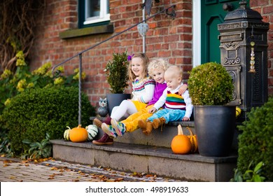 Group of little children sitting on stone stairs to the house door on warm autumn day during Halloween or Thanksgiving time. Kids playing in the front yard in fall. Home porch decorated with pumpkins.
