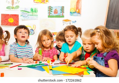 Group of little kids painting with pencils and gluing with glue stick on art class in kindergarten