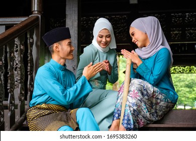 A group of malay muslim people in traditional costume showing greeting gesture during Aidilfitri celebration at terrace of traditional wooden house