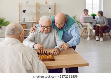 Group of a male elderly senior people playing chess in nursing home sitting at the table. Pensioners spending leisure time together playing board games. Leisure in retirement home concept. - Powered by Shutterstock