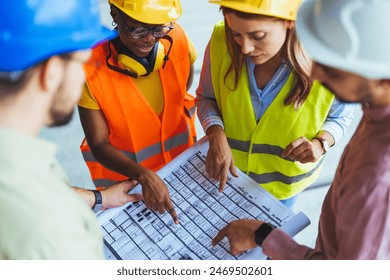 A group of male and female construction workers, clad in hard hats and reflective vests, are engaged in reviewing architectural plans on the job site. - Powered by Shutterstock