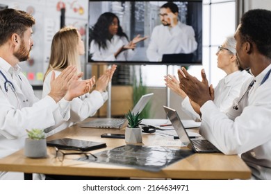 Group Of Male And Female Doctors Cheering With Applause Their Multicultural Colleagues During Online Medical Presentation At Clinic. Focus On Modern Digital Screen.