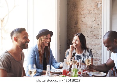 Group of male and female friends or couples having a good time at dinner table with plates and wine glasses near large bright window - Powered by Shutterstock