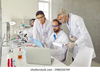 Group of male and female lab technicians and scientists working in laboratory together, doing professional medical research, using laptop, looking at scientific data report, discussing analysis result - Powered by Shutterstock