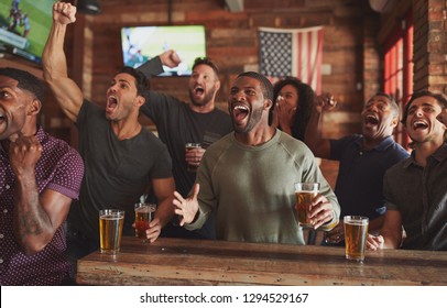 Group Of Male Friends Celebrating Whilst Watching Game On Screen In Sports Bar