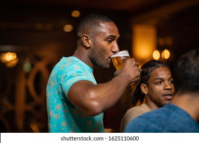 A group of male friends drinking together in a bar. The main focus is on a man drinking a pint of beer.  - Powered by Shutterstock